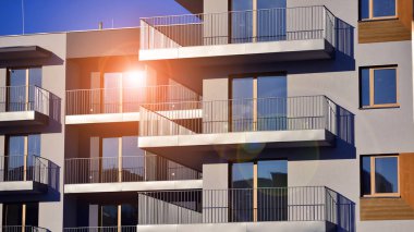 Şık yüzlü ve geniş pencereli modern konut binası. Büyüyen bir mahallede çağdaş şehir mimarisi. Güneşli bir gökyüzünün altında gayrimenkul gelişimi.