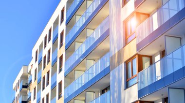 Şık yüzlü ve geniş pencereli modern konut binası. Büyüyen bir mahallede çağdaş şehir mimarisi. Güneşli bir gökyüzünün altında gayrimenkul gelişimi.