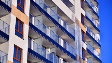 Şık yüzlü ve geniş pencereli modern konut binası. Büyüyen bir mahallede çağdaş şehir mimarisi. Güneşli bir gökyüzünün altında gayrimenkul gelişimi.