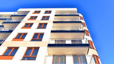 Şık yüzlü ve geniş pencereli modern konut binası. Büyüyen bir mahallede çağdaş şehir mimarisi. Güneşli bir gökyüzünün altında gayrimenkul gelişimi.