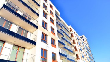 Şık yüzlü ve geniş pencereli modern konut binası. Büyüyen bir mahallede çağdaş şehir mimarisi. Güneşli bir gökyüzünün altında gayrimenkul gelişimi.