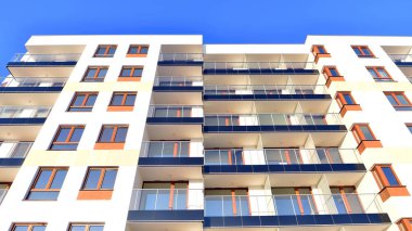 Şık yüzlü ve geniş pencereli modern konut binası. Büyüyen bir mahallede çağdaş şehir mimarisi. Güneşli bir gökyüzünün altında gayrimenkul gelişimi.