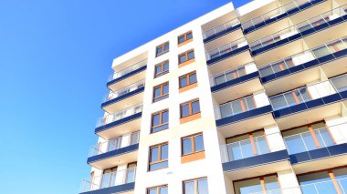 Şık yüzlü ve geniş pencereli modern konut binası. Büyüyen bir mahallede çağdaş şehir mimarisi. Güneşli bir gökyüzünün altında gayrimenkul gelişimi.