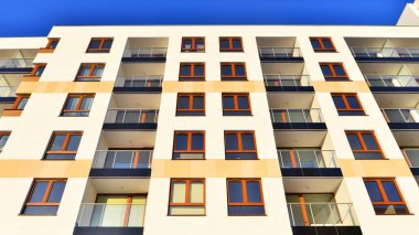 Şık yüzlü ve geniş pencereli modern konut binası. Büyüyen bir mahallede çağdaş şehir mimarisi. Güneşli bir gökyüzünün altında gayrimenkul gelişimi.