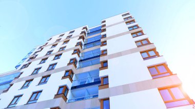 Şık yüzlü ve geniş pencereli modern konut binası. Büyüyen bir mahallede çağdaş şehir mimarisi. Güneşli bir gökyüzünün altında gayrimenkul gelişimi.