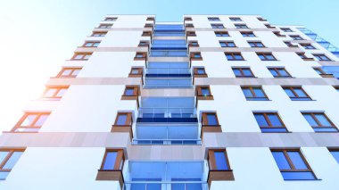 Şık yüzlü ve geniş pencereli modern konut binası. Büyüyen bir mahallede çağdaş şehir mimarisi. Güneşli bir gökyüzünün altında gayrimenkul gelişimi.