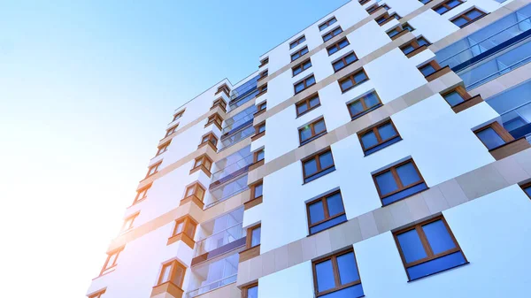 Şık yüzlü ve geniş pencereli modern konut binası. Büyüyen bir mahallede çağdaş şehir mimarisi. Güneşli bir gökyüzünün altında gayrimenkul gelişimi.