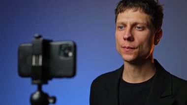 Takım elbiseli genç adam akıllı telefondan sosyal medya içeriğini kaydediyor rgb renkli arka plan stili modern kurulum.