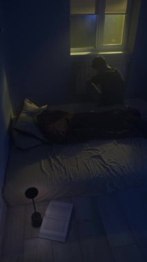 Kalbi kırık bir adam karanlık bir odada yatakta oturuyor, ayrılık, üzüntü ve yalnızlıkla boğuşuyor..