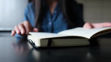 Evdeki kağıt bir defterde sayfaları çeviren bir kızın yakın plan resmi. Masadaki sıradan gerçek hayat anı.