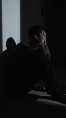 Karanlık bir köşede, sessiz bir çöküşe doğru kayan, elleri başının üstünde, iç acı ve paniğe boğulmuş bir adam. Sessiz çöküntü, zihinsel sağlık krizi.