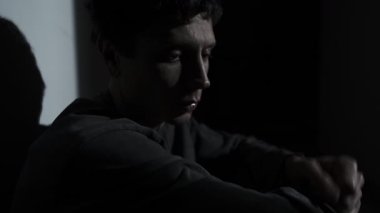 Adam karanlık bir odada oturur ve kendi kendine fısıldar. Stres, iç çatışma ve aşırı duygusal yüklenme gösterir. İç diyalog, endişe ve psikolojik kriz kavramı.