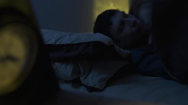 Yorgun bir adam uyuyamıyor, geç saatlere kadar saate bakıyor. Uykusuzluk ve uyku sorunları kavramı.