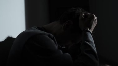 Kafası aşağıda stresli bir adam, karanlık bir odada rahatsız edici düşüncelerle savaşırken saçlarını tutuyor. Gerçek zihinsel mücadele, korku, aşırı düşünme, panik..