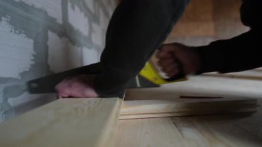 Yerdeki döşeme montajı sırasında tahta kesen bir işçinin yakın çekimi. Gerçek elle inşa süreci