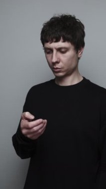 Telefondan yayın yapan adam, stüdyonun gri arka planında endişeli ve dikkati dağılmış hissediyor.