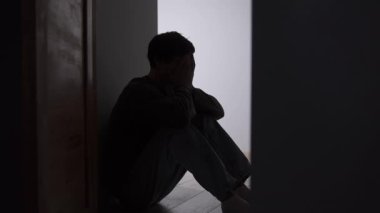 Yalnız adam silueti, karanlık koridorda, aydınlık kapısında oturuyor. Duygusal sıkıntı, izolasyon, iç mücadele, belirsizlik ve kırılgan zihinsel durum gösteren isimsiz bir erkek figürü..