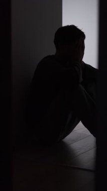 Yalnız adam silueti, karanlık koridorda, aydınlık kapısında oturuyor. Duygusal sıkıntı, izolasyon, iç mücadele, belirsizlik ve kırılgan zihinsel durum gösteren isimsiz bir erkek figürü..