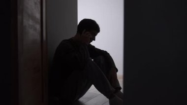 İlişki çatışması sırasında duygusal telefon görüşmesi. Karanlık koridorda oturmuş akıllı telefondan konuşan stresli erkek silueti. Yoğun sohbet, duygusal gerilim, erkek hassasiyeti ve akıl sağlığı.