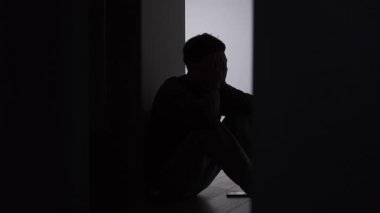 Telefon görüşmesinden sonra, akıllı telefon yerde yalnız bir adamın siluetinin yanında, karanlık koridorda oturuyor, baş ellerde, çatışma üstüne sessizlik, duygusal yorgunluk, bozuk iletişim anı..