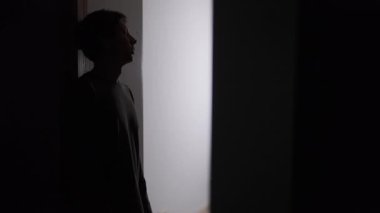 Duygusal baskı altında kapı eşiğinde duran bir adam, elleri yüzü parlak bir ışığa bakan bir siluet, yaşam krizi anı, aşırı stres ve kişisel karar verme zorluğu.