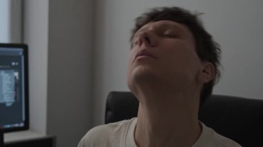 İş molasında ofis koltuğunda boyun egzersizi yapan genç bir adam. Uzaktan kumandalı bilgisayar, sağlıklı yaşam tarzı ve yerleşik iş önleme.