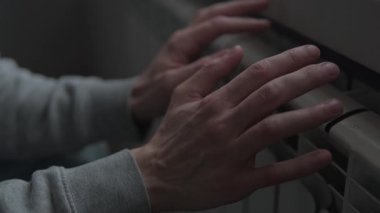 Evde ısıtma yok, adam soğuk dairede radyatörün yanında ellerini ısıtıyor, enerji krizi yaşam tarzı.