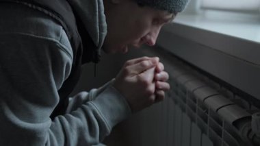 İnsani kriz konsepti, soğuk dairede radyatörün yanında elini ısıtan adam, enerji kıtlığı ve ısıtma sistemi hatası, küresel istikrarsız yaşam tarzı