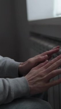 Evde ısıtma yok, adam soğuk dairede radyatörün yanında ellerini ısıtıyor, enerji krizi yaşam tarzı.