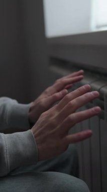 İnsani kriz konsepti, soğuk dairede radyatörün yanında elini ısıtan adam, enerji kıtlığı ve ısıtma sistemi hatası, küresel istikrarsız yaşam tarzı