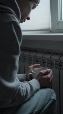 Evde enerji krizi, soğuk bir dairede sıcak tutmak için kaloriferin yanında sıcak çay tutan ellerin kapatılması, yüksek ısıtma giderleri ve günlük yaşam tarzı.