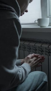 İnsani kriz konsepti, soğuk dairede radyatörün yanında elini ısıtan adam, enerji kıtlığı ve ısıtma sistemi hatası, küresel istikrarsız yaşam tarzı