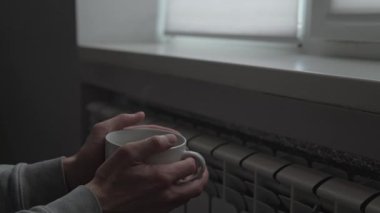 Soğuk bir yaşam tarzı, sıcak çay içen bir adam kış boyunca ısınmak için radyatörün yanında, gerçek bir ev.