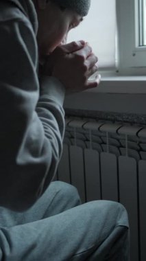 Evde enerji krizi, radyatörün yanında oturan adam soğuk bir dairede sıcak çay içiyor, yükselen ısıtma fiyatları ve basit kış yaşam tarzı.