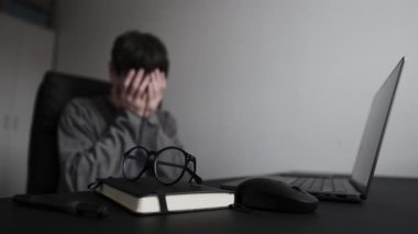 Beklenmedik proje başarısızlığı tepkisi, ofis masasındaki adam elleriyle yüzünü kapatıyor, iş aksiliği ve stresle başa çıkıyor.