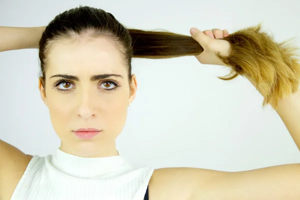 Krásný ženský model tahání dlouhé vlasy v culíku hledá vážné kamery záběr — Stock fotografie