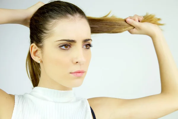 Schönes weibliches Modell, das lange Haare in Pferdeschwanz zieht, sieht ernst aus — Stockfoto