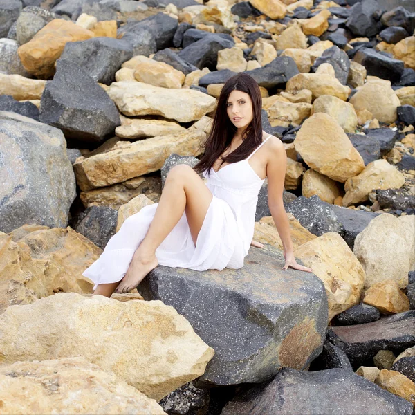 Fastuos doamnă cu rochie albă pozând așezat pe pietre zâmbind camera medie shot — Fotografie, imagine de stoc