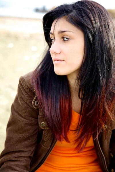 Girl thinking sitting on beach with red and black hair — Stock Photo, Image