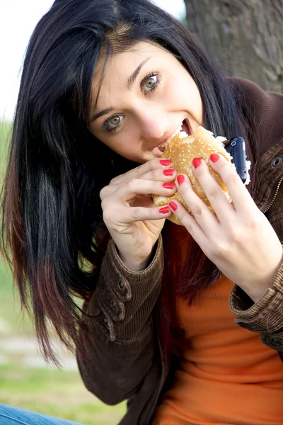 Hungry for technology eating hamburger with smart phone — Stock Photo, Image