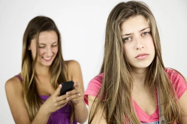 Adolescente feminina muito triste enquanto a namorada está rindo com o telefone celular — Fotografia de Stock