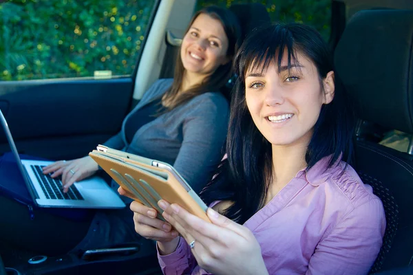 Två glada affärskvinnor arbetar i bil med teknik — Stockfoto
