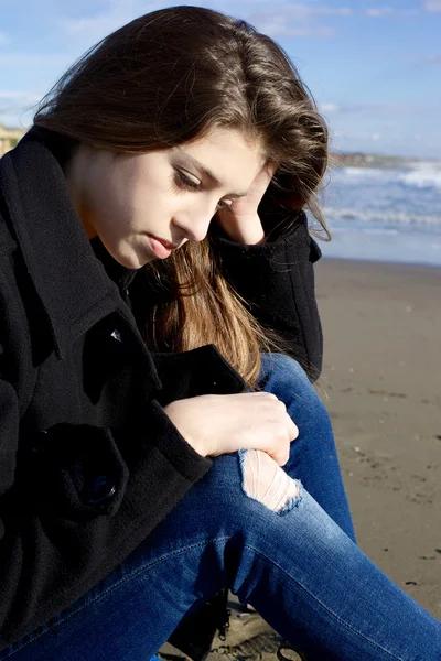 Грустная девушка думает, сидя на пляже зимой — стоковое фото