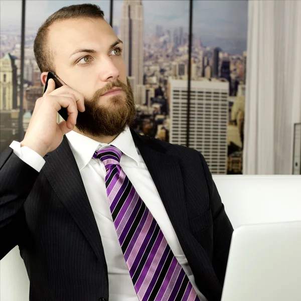 Hombre de negocios guapo con barba trabajando en la oficina en el ordenador portátil y el teléfono celular — Foto de Stock