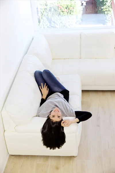 Ung kvinna liggande på rygg i soffan tittar på kameran leende — Stockfoto