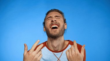 young bearded man with closed eyes gesturing while laughing on blue  clipart