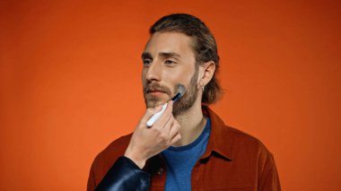 Makyaj sanatçısı portakallı genç adama yüz pudrası uyguluyor.