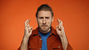 bearded young man with crossed fingers on orange  clipart