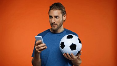 Mavi tişörtlü, akıllı telefon kullanan ve futbol topunu turuncu üzerinde tutan bir futbol taraftarı şaşırdı. 