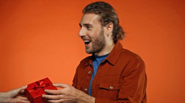 happy young man receiving wrapped present on orange  clipart
